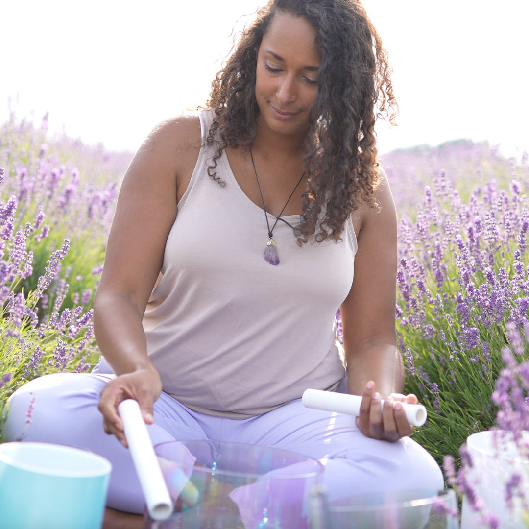 woman sitting in lavender field playing crystal singing bowls 