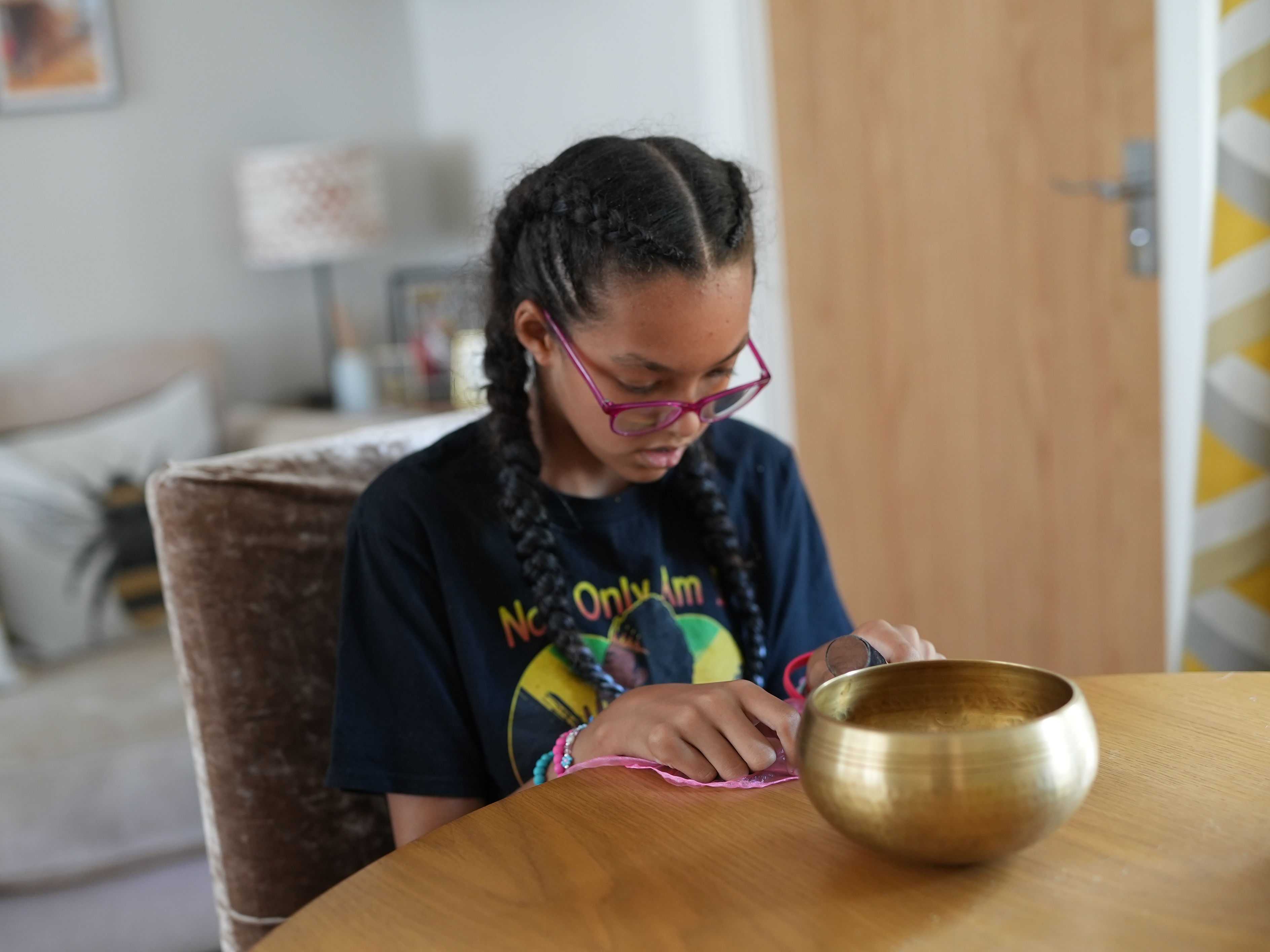 Teenage girl with additional needs wearing a black top sits at a wooden table with a pink sensory silk scarf and tibetan bowl