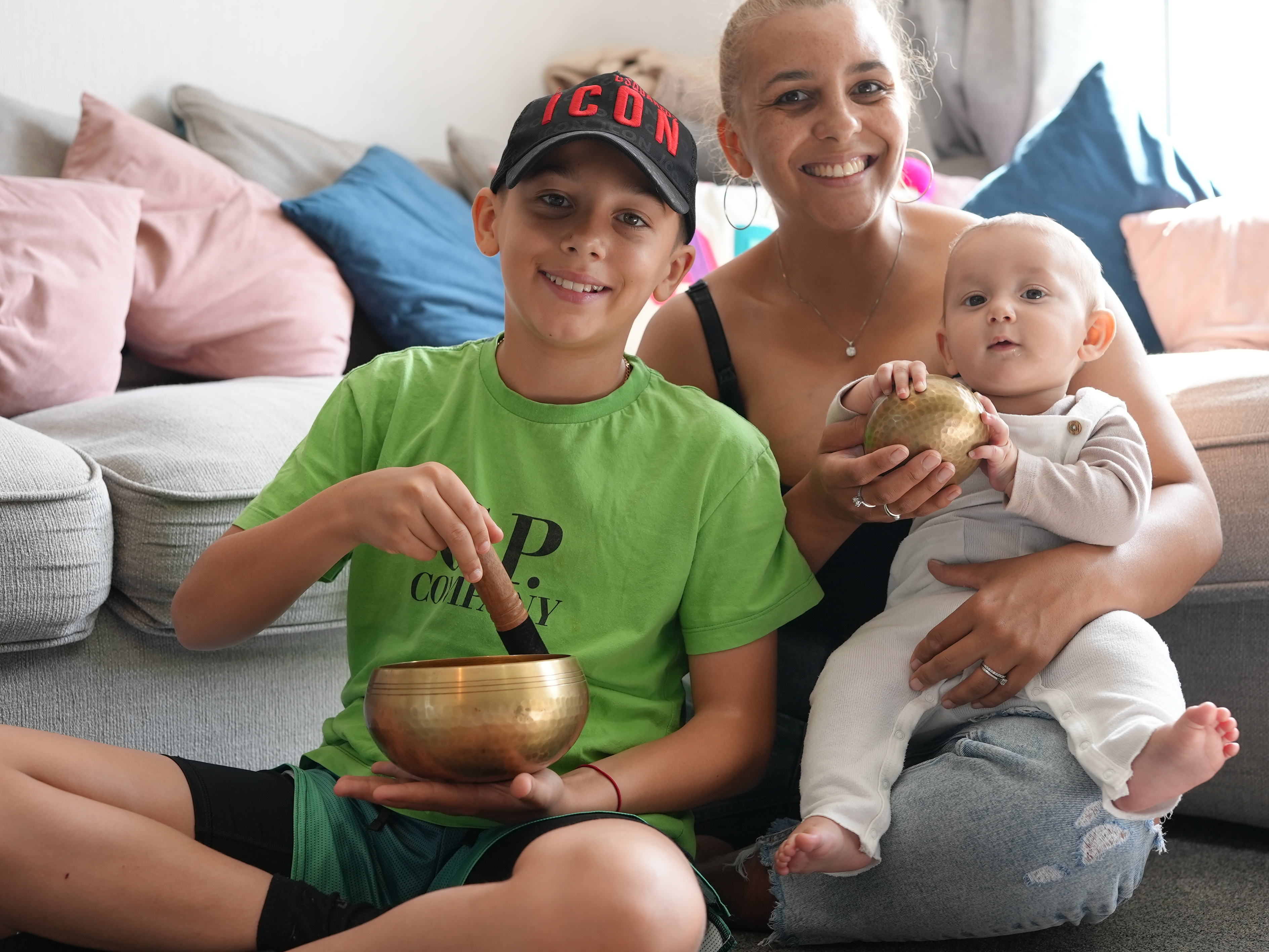 Mother with young son and baby boy smile as they play with tibetan bowls