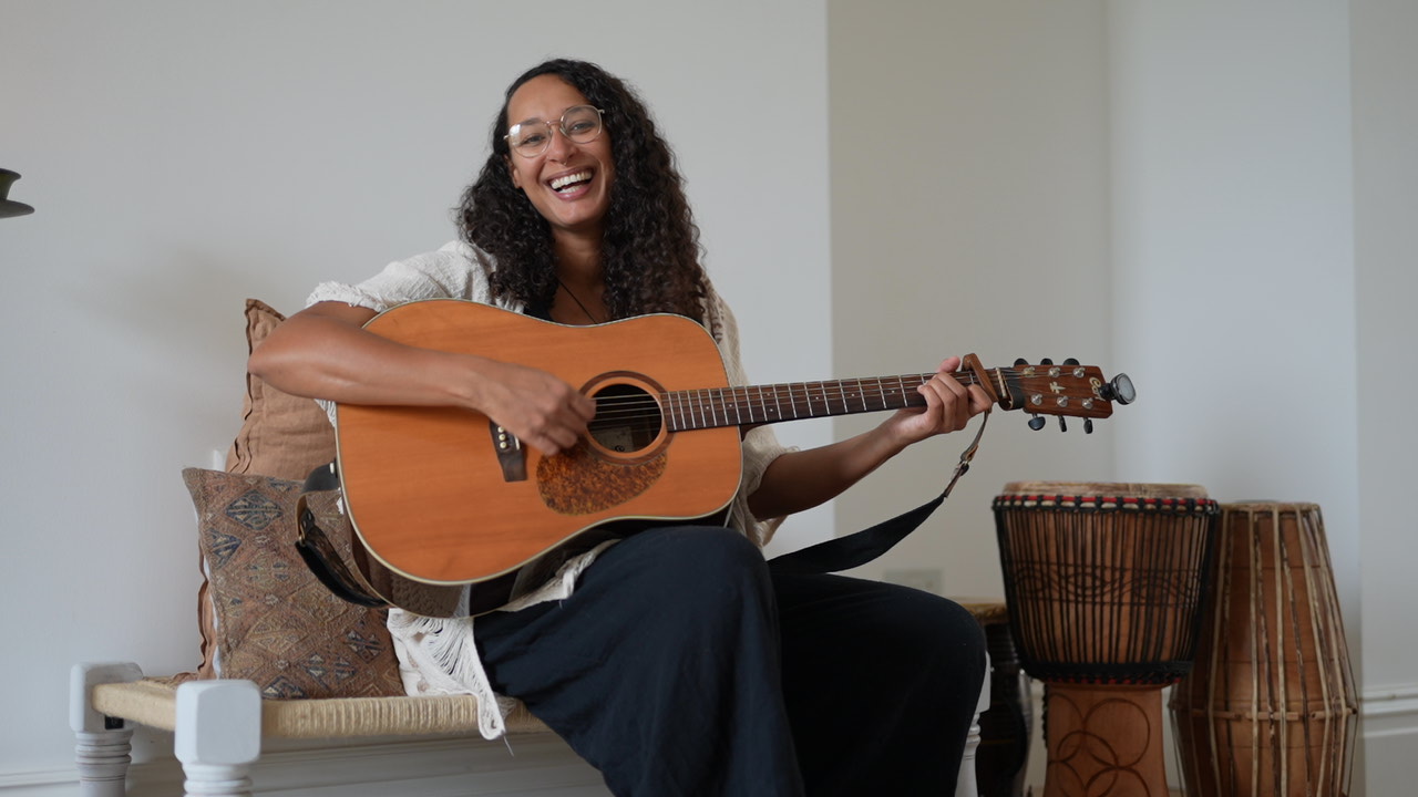woman sitting playing guitar smiling